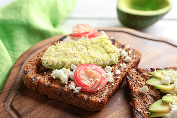 Tasty toasts with avocado on wooden board