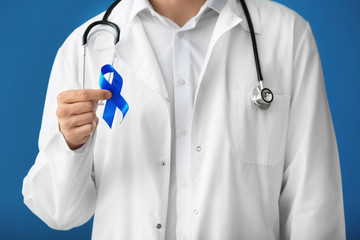 Doctor holding blue ribbon on color background, closeup. Prostate cancer concept