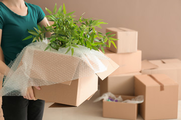 Woman holding carton box with houseplants indoors. Moving house concept