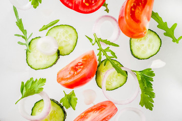 Creative background, layout, concept of fresh healthy diet of salad, fresh raw  vegetables tomatoes parsley onions cucumbers greens, simple pattern on white background