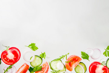 Creative background, layout, concept of fresh healthy diet of salad, fresh raw  vegetables tomatoes parsley onions cucumbers greens, simple pattern on white background