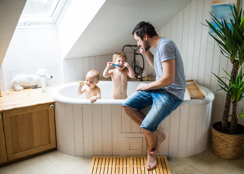 Father with two toddlers brushing teeth in the bathroom at home.