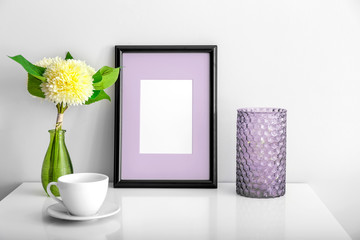 Composition with photo frame on table against light wall