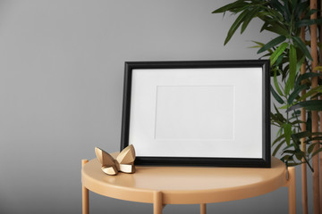 Photo frame on table near green plant against color background