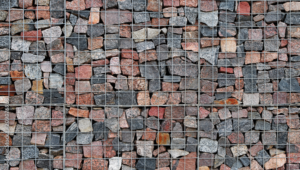 Wall mural fragment of grey metal wire fence filled with rocks as abstract colorful stone textured background.