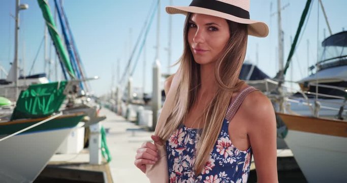 Portrait of attractive woman in summer outfit posing outside near docked boats, Stylish attractive woman in her 20s wearing fedora and romper standing on marina, 4k