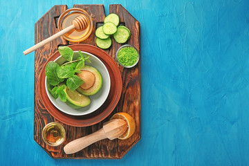 Wooden board with avocado and ingredients for natural homemade cosmetics on color background