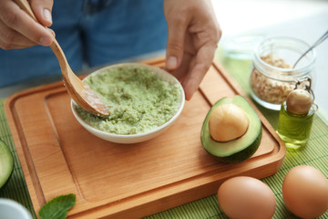 Young woman making nourishing mask with avocado at table