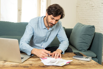 angry man paying bills as home with laptop and calculator