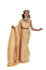 full length portrait of brunette woman wearing long golden grecian gown. standing pose on white studio background.