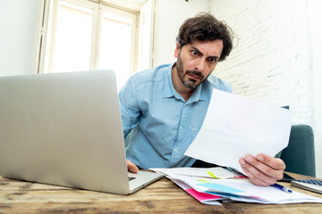 angry man paying bills as home with laptop and calculator