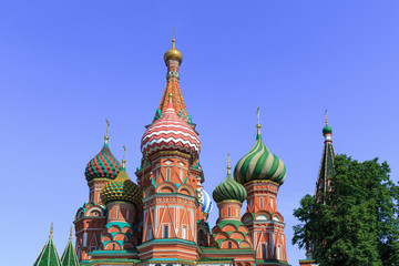 Fototapeta na wymiar Domes of St. Basil's Cathedral against green trees and blue sky on a sunny summer morning