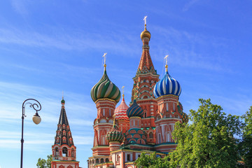 Domes of St. Basil's Cathedral in Moscow against green trees and blue sky on a sunny summer morning