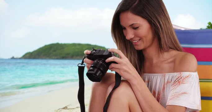 Pretty girl taking photo with camera while sitting at beach on tropical vacation, Young Caucasian female photographer in her 20s sitting in chair at beach taking photo, 4k