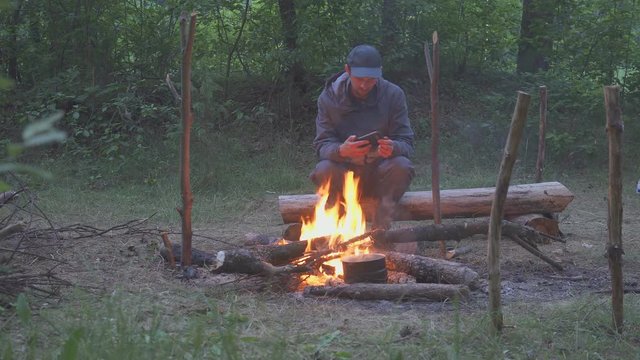 A freelancer man touch a smartphone near tourist campfire in evening