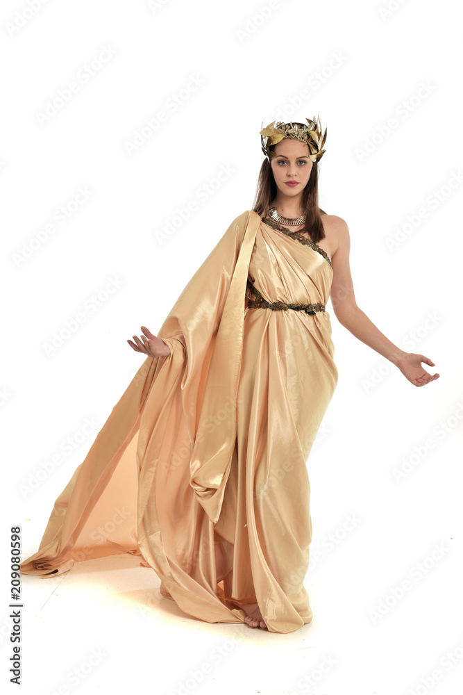 Wall mural full length portrait of brunette woman wearing long golden grecian gown. standing pose on white studio background.