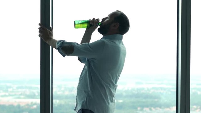 Drunk man drinking beer by window at home
