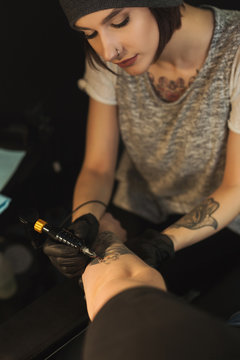 Young woman tattooist doing tattoo on male arm