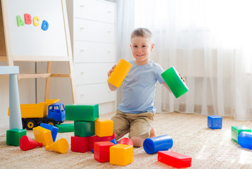 5 years old boy sitting on the floor playing with colorful plastic blocks. Creativity educational toys for preschoolers