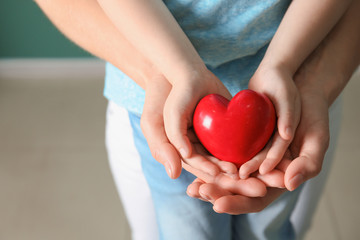 Hands of mother and child with red heart, closeup