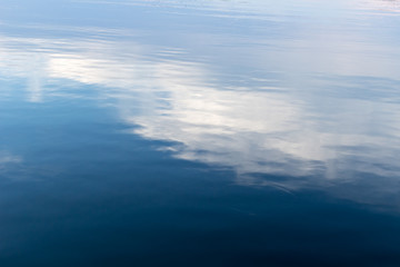 Obraz premium Abstract reflection of clouds on the surface of water. Shades of blue and white reflect on a lake creating a diagonal pattern. 