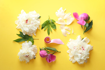 Composition with beautiful peony flowers and ribbon on color background