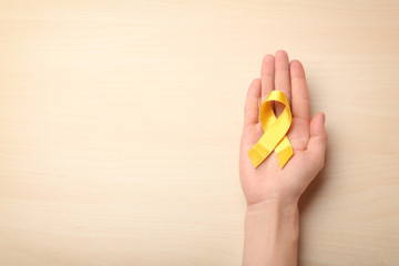 Female hand holding yellow ribbon on light background. Cancer concept