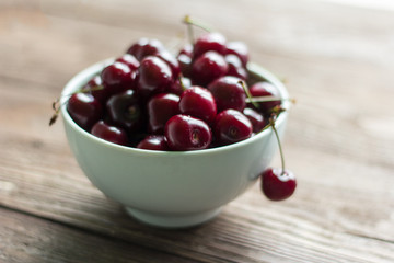 fresh, ripe, juicy cherries in a white bowl on a wooden background with a shallow depth of field, selective focus