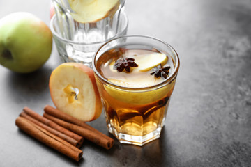Tasty drink with cinnamon and apple slices in glass on grey background