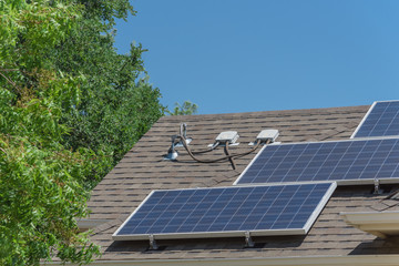 Close-up solar panel system on asphalt shingles rooftop surround green tree. End run, junction box, enclosure bracket installation at Grapevine, Texas, USA. Rail-less racking module, renewable energy