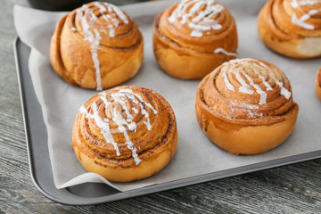 Tray with delicious cinnamon buns on wooden background, closeup