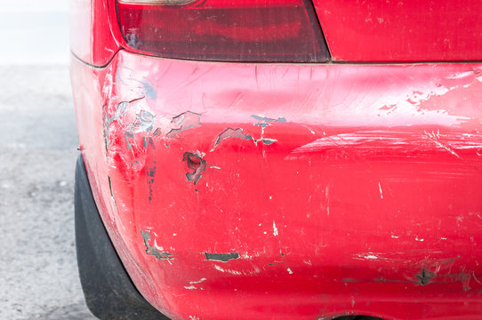 Red damaged car in crash accident with scratched paint and dented rear bumper metal body