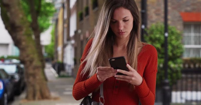 Young woman taking phone out of purse to send text while standing on sidewalk, Young lady pulling smartphone out of bag to reply to text standing outside in neighborhood, 4k