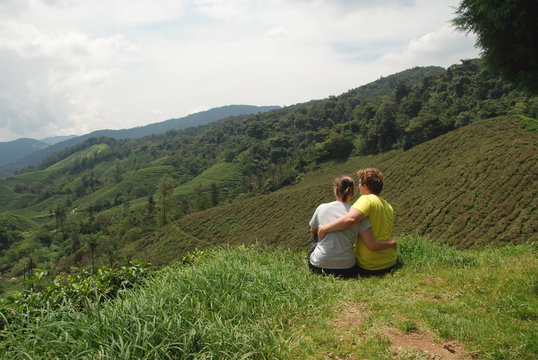 A Young Couple Of Travelers Sitting And Looking At Tea Plantations Of Cameron Highlands In Malaysia