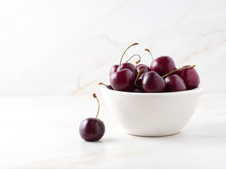 red dark sweet cherries in white bowl on stone white table, side view, copy space
