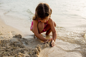 Cute little girl playing with sand and building sandcastle on the beach in Dubai