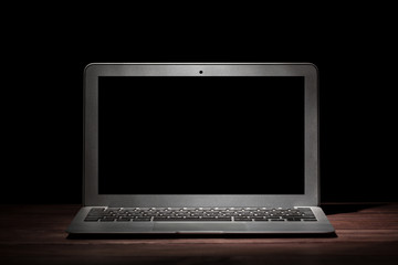 One silver modern laptop on wooden table in a dark room on black background. Nice mockup for your...
