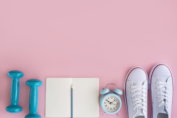 White sneakers, notebook, dumbbells and tape measure on pink background