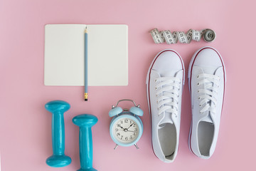 White sneakers, notebook, dumbbells and tape measure on pink background