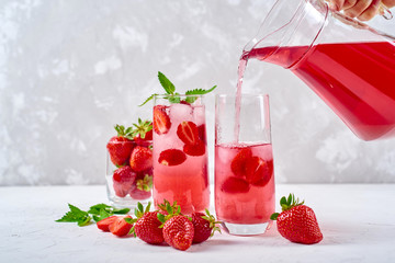 Woman pours strawberry lemonade in glass. Cocktail with strawberry, ice and mint in glasses on...