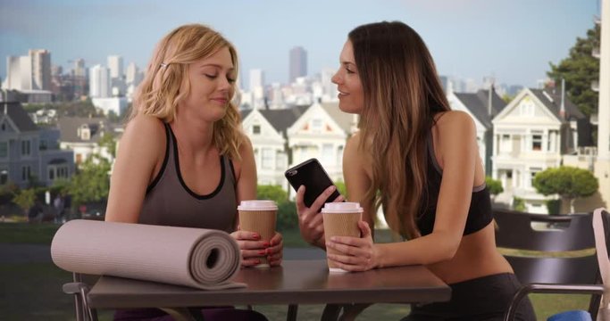 Cute attractive women with yoga mats looking at smartphone in front Painted Ladies San Francisco, Lovely caucasian woman showing yoga partner cell phone in residential area, 4k 