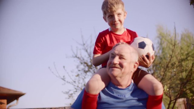 Portrait of grandpa with his grandson on the neck with soccer ball