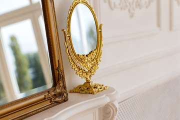 Close-up two mirrors in vintage style stand on a mantel bolt in a white baroque room