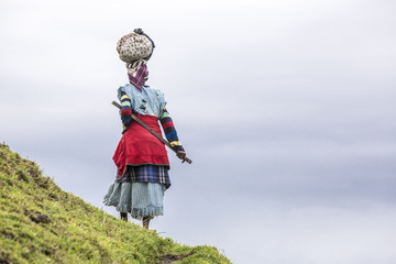 Native black African woman carries a load on her head in the hills of South Africa