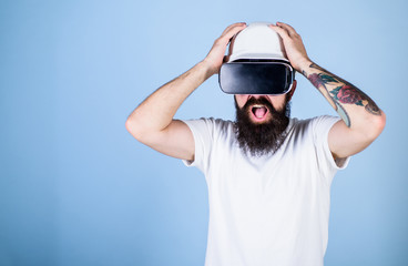 Guy in helmet works as engineer in virtual reality. 3D design concept. Man with beard in VR glasses shocked and disappointed, light blue background. Architect or engineer with virtual reality glasses