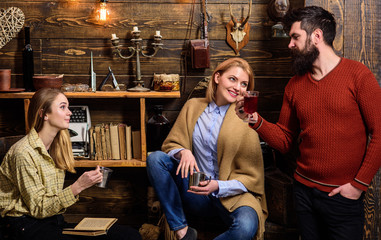 Friends, family spend pleasant evening, interior background. Girls and man on happy faces hold metallic mugs, enjoy coziness with drinks. Coziness concept. Friends drinking tea and chatting