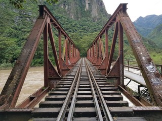 puente de metal sobre rió con vía férrea en dirección a un bosque