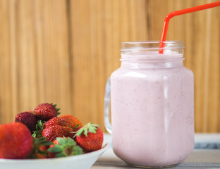 Healthy strawberry cocktail on a wooden background with ripe berries on a plate