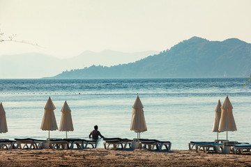 Fototapeta na wymiar White umbrellas, blue sea and big mountains on horizon