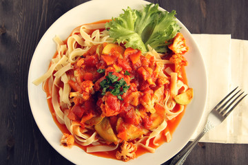 Ribbon pasta with Arrabiata sauce. Close up. Mediterranean dish. Tagliolini pasta with vegetables. Cauliflower, courgette and tomato stew. Italian cuisine. Vegan and vegetarian. Top view.